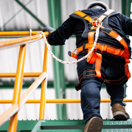 Man climbing construction scaffolding in a safety harness, performing jobsite safety analysis.