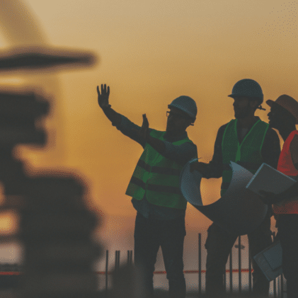Three construction contractors standing together at an active worksite, discussing the project.