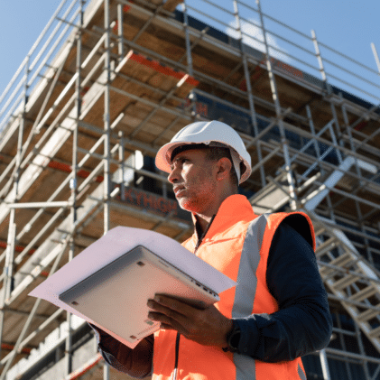 GC standing at construction site looking over schedule of values print out.
